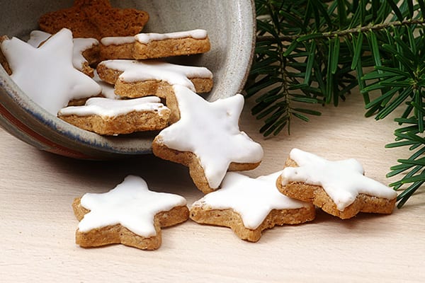 Neben einem Tannenzweig liegen Weihnachtsplätzchen in Sternform.