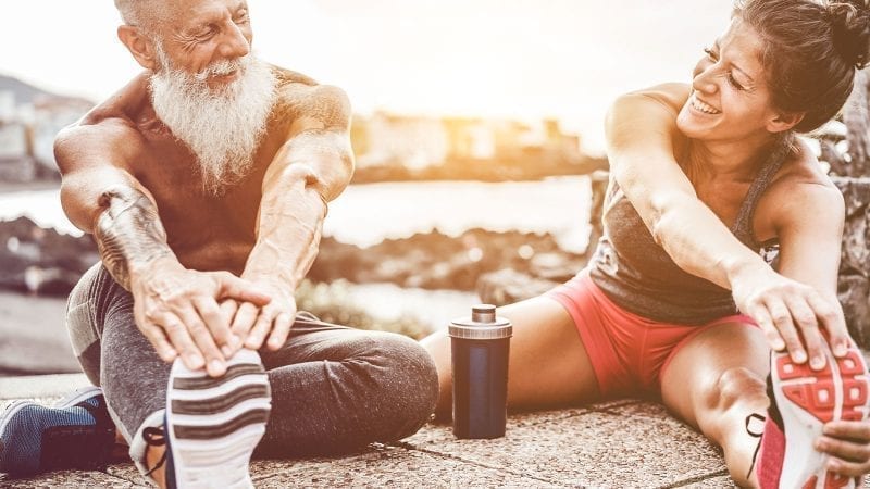 Aelterer Sportler und junge Sportlerin bei Dehnuebungen